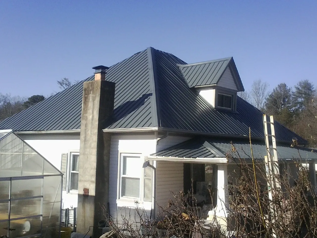 Dark blue standing seam metal roof on a white farmhouse with dormer — Slate & Tile Roof Repair by Roofing Brothers in East Vandergrift