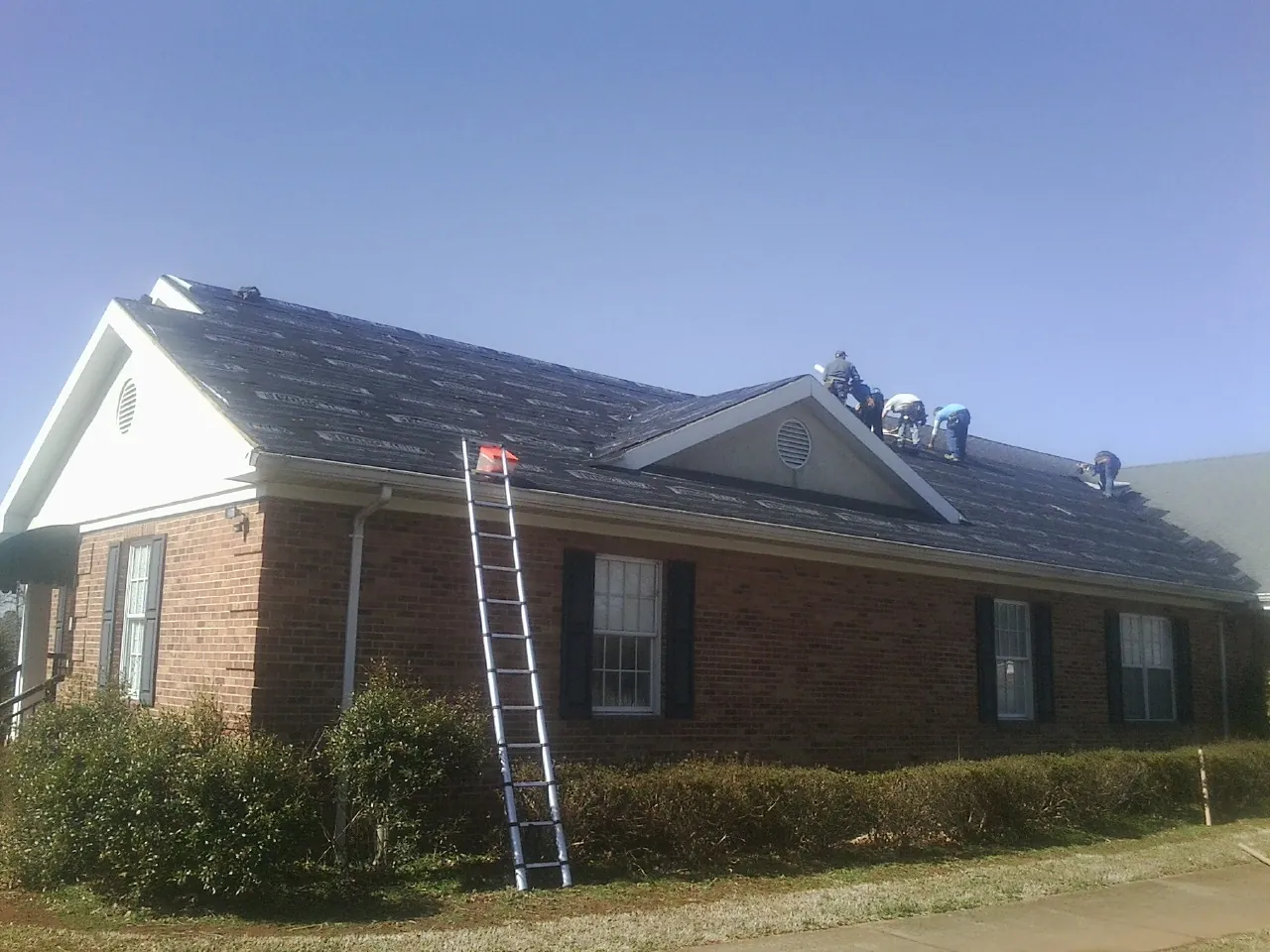 Crew tearing shingles off a brick ranch roof with a ladder set — Metal Roof Repair work by our crew in East Vandergrift