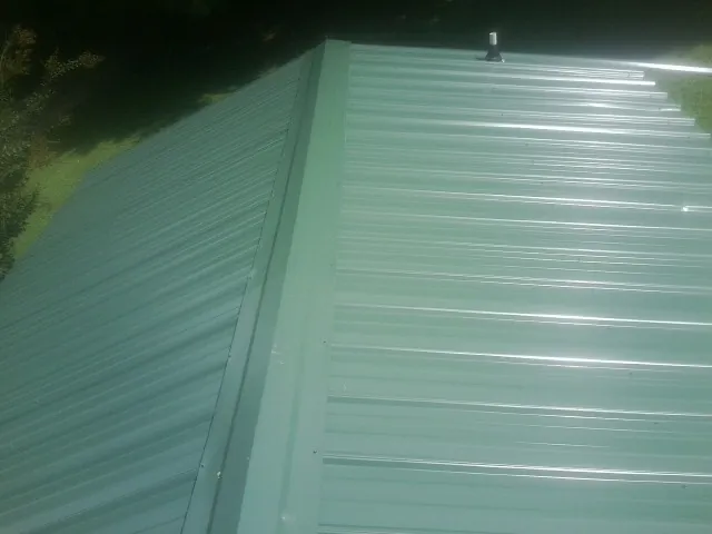 New green metal panels meeting at the ridge of a roof — Flat Roof Repair work by our crew in East Vandergrift