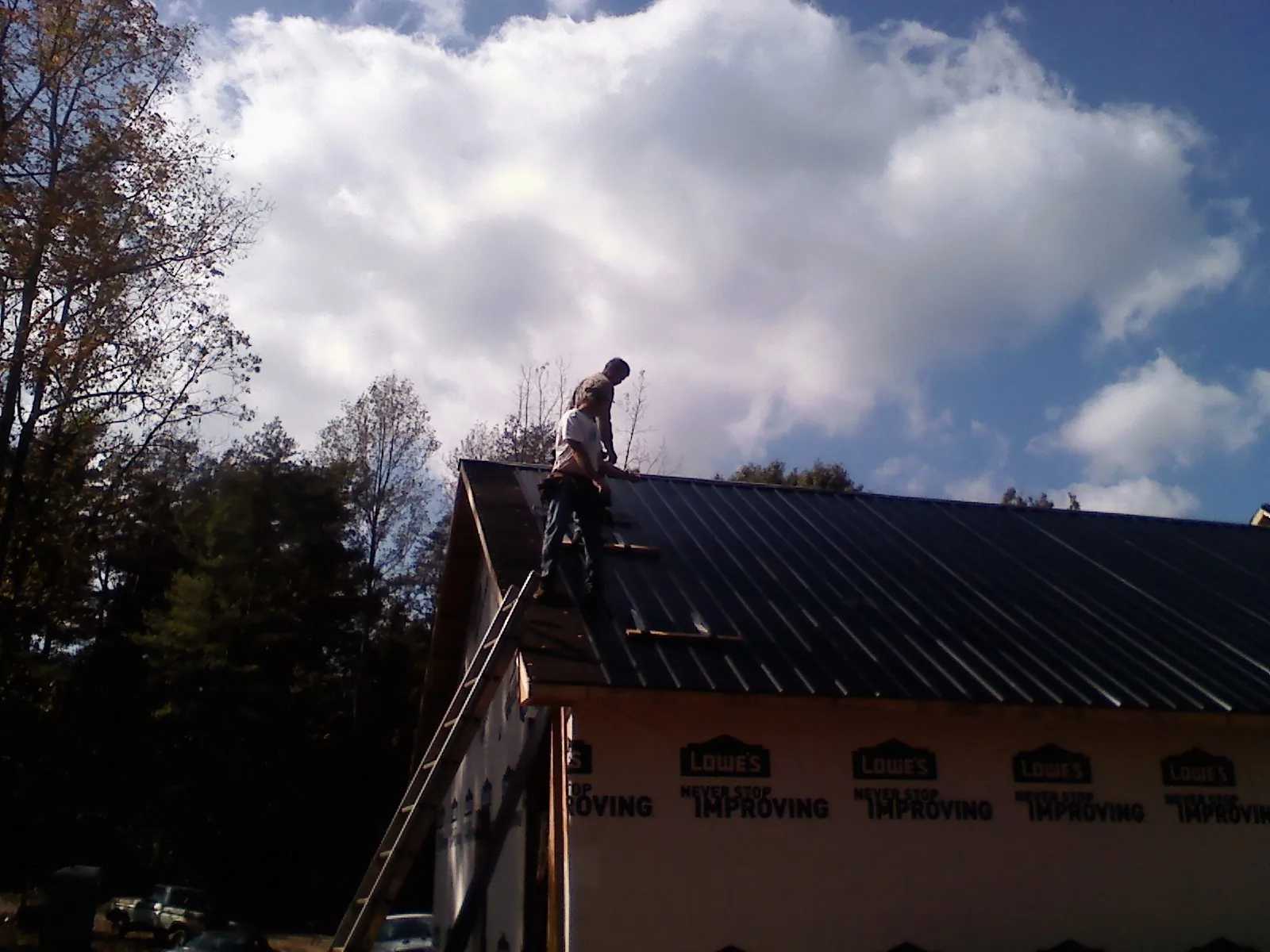 Roofer fastening dark metal panels high against a cloudy sky, from a Roof Inspection job in East Vandergrift