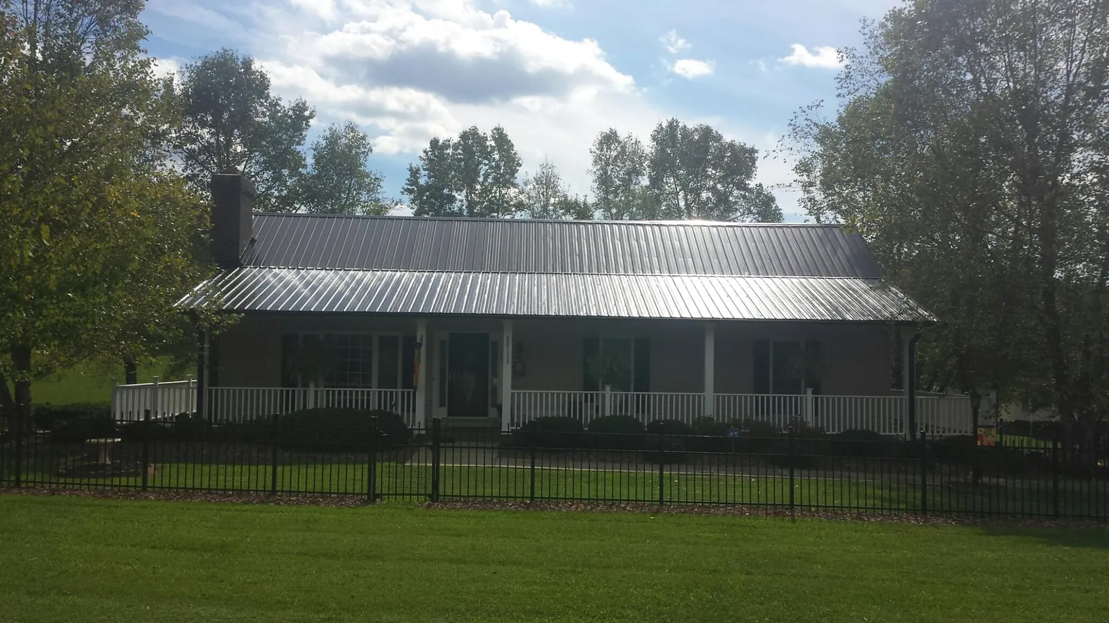 Gray metal roof on a brick ranch with a full width front porch — Gutter Guard Installation work by our crew in East Vandergrift
