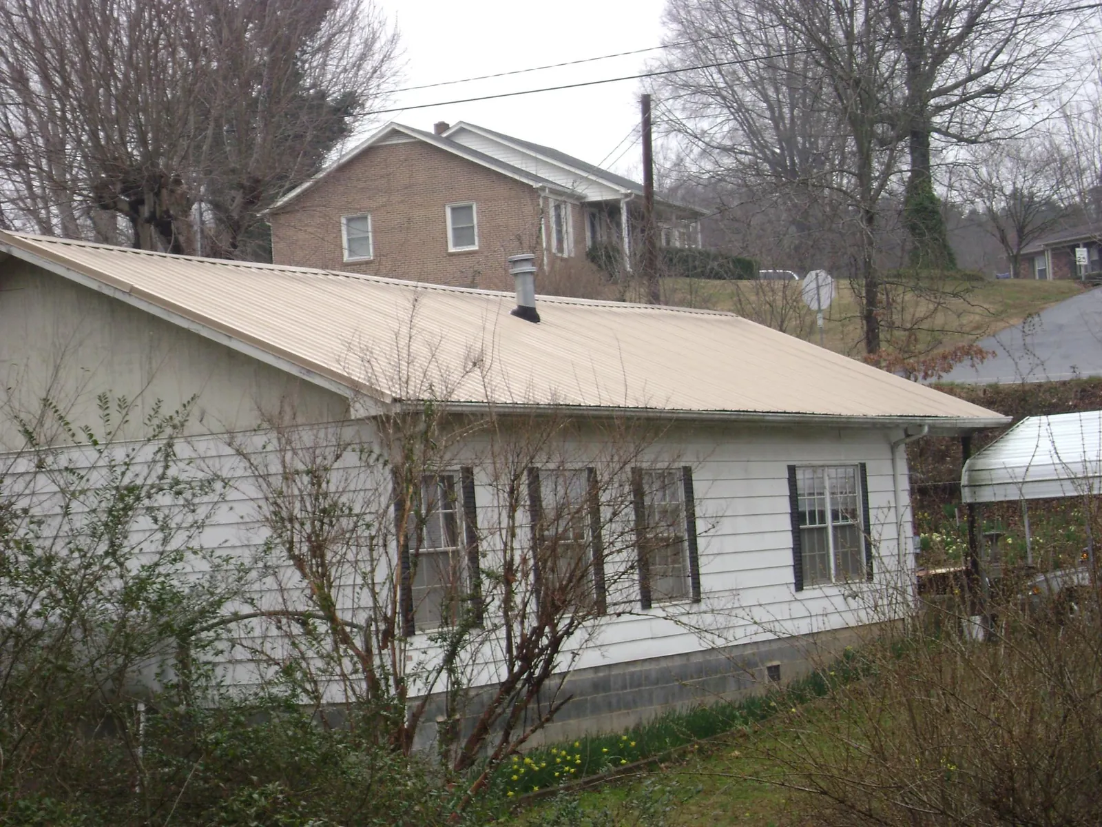 Tan metal roof on a white sided house set into a hillside — Commercial Roofing by Roofing Brothers in East Vandergrift